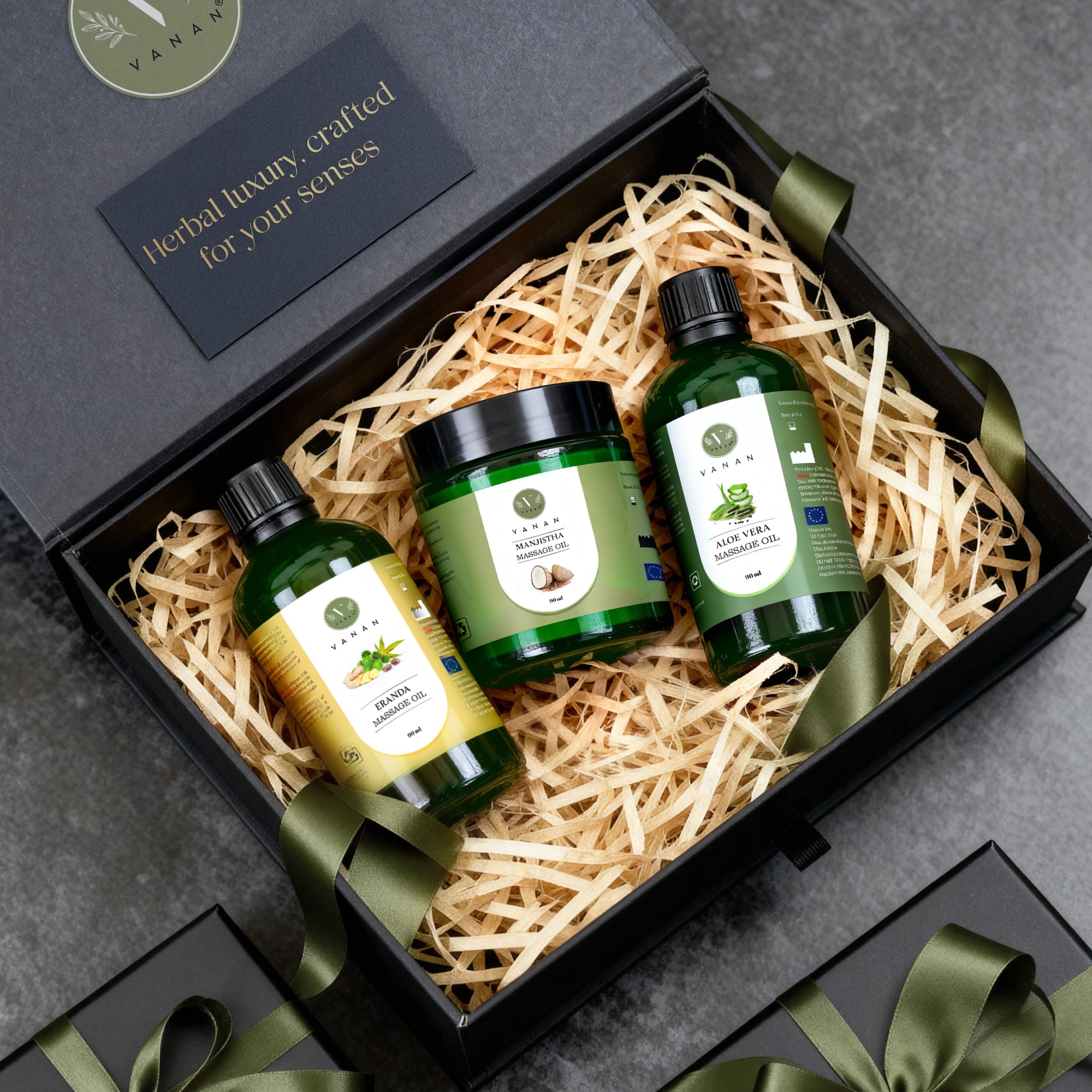 Three green bottles in a gift box with decorative ribbons on a gray surface.